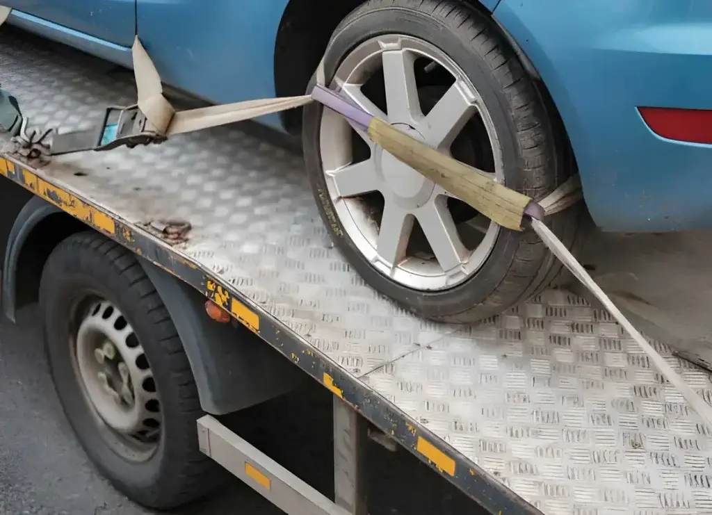 Soft yellow strap secured over a car wheel on a flatbed tow truck ramp