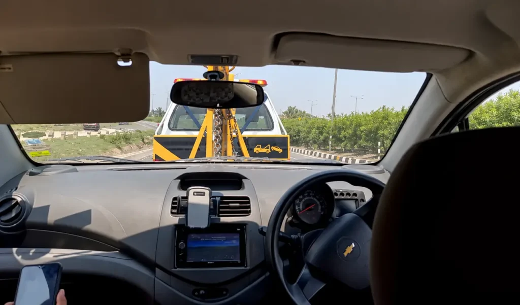 Tow truck with amber lights approaching, seen in a car rearview mirror on a sunny highway
