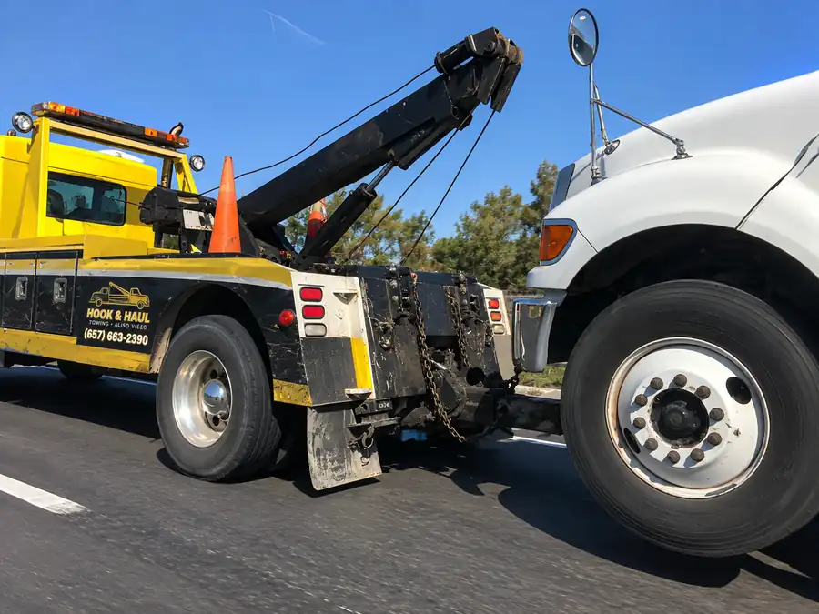 Yellow Hook & Haul wheel-lift tow truck with its boom raised on a sunny highway